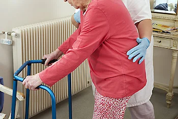 Healthcare professional assisting an older adult using a walker.