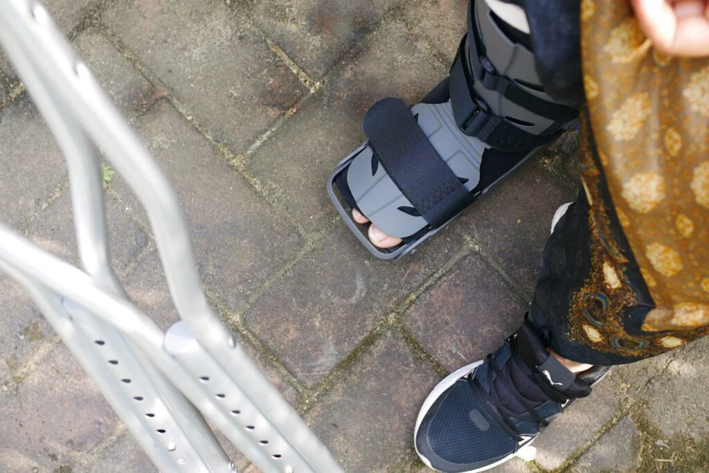Person wearing a walking boot and using crutches.