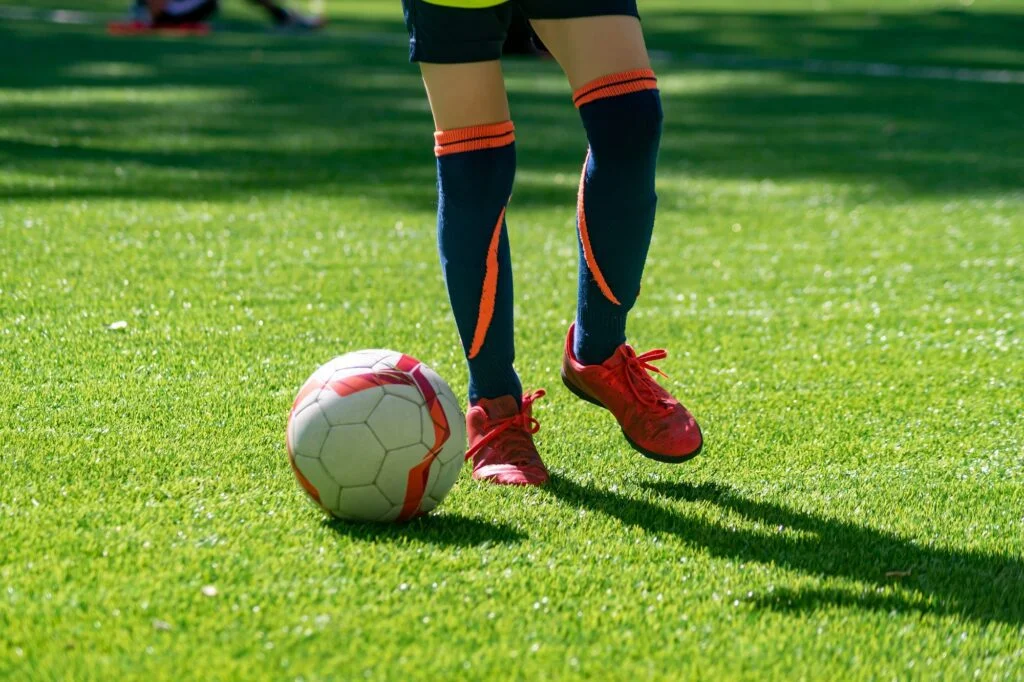 Soccer player dribbling a ball on a grass field, representing sports foot and ankle care.